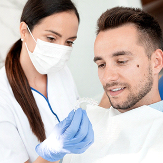 A dentist showing a male patient an Invisalign aligner in preparation for his fitting