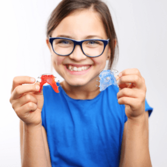 Teen girl holding up red and blue retainers